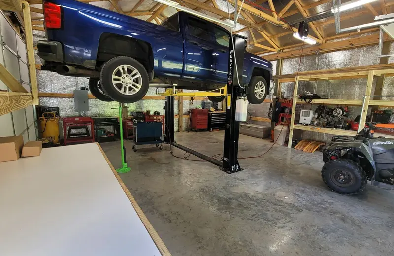 A pickup truck raised on the two-post lift inside the shop